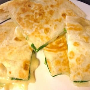 An overhead view of Four triangle slices of a Spinach and Brie Quesadilla on a plate