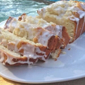 Limoncello Cake topped with Limoncello Glaze cut into slices on a square plate with a pool in the background