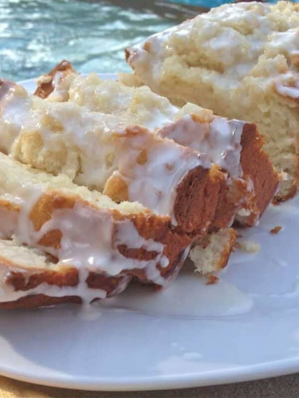 Limoncello Cake topped with Limoncello Glaze cut into slices on a square plate with a pool in the background