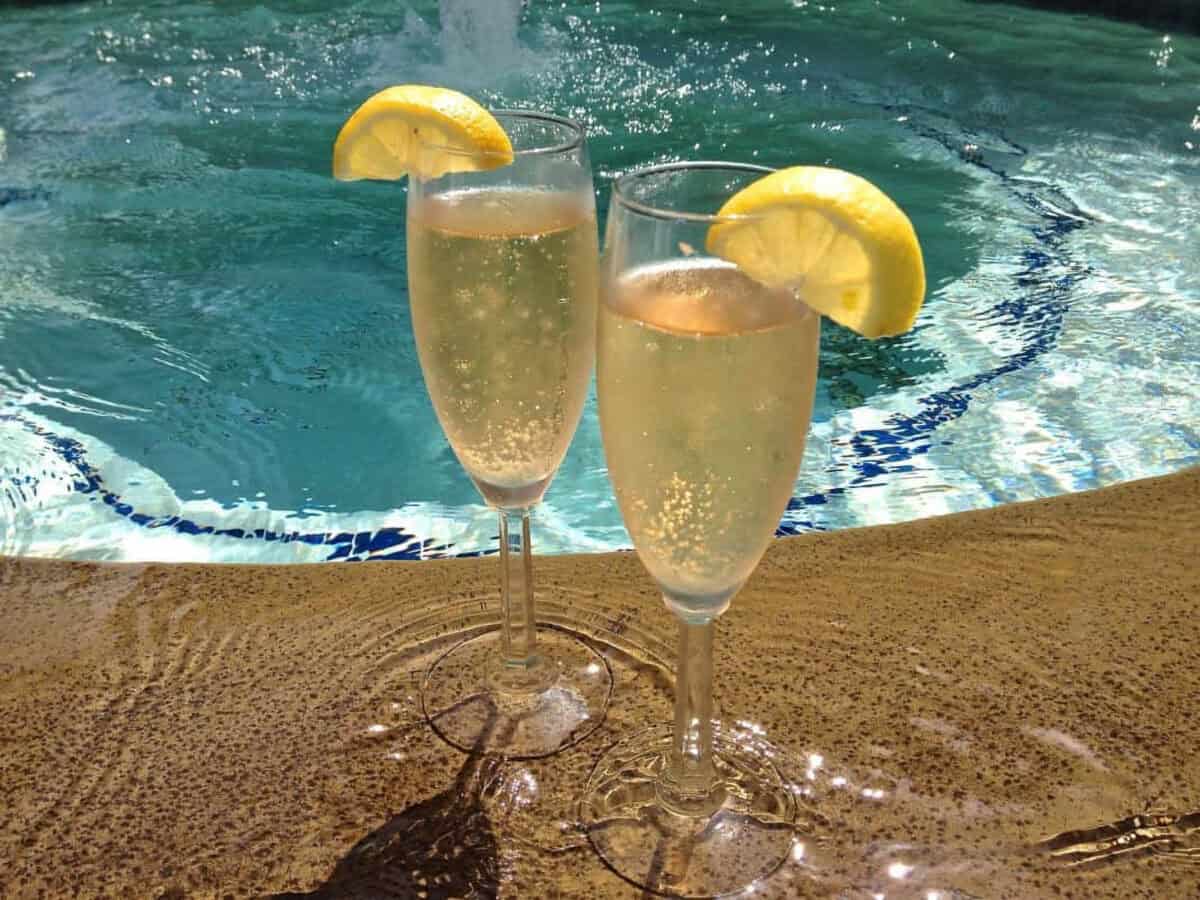 Champagne Limoncello Aperitifs via Zagleft Two champagne flutes of Limoncello Champagne Aperitifs garnished with a lemon slice with a pool in the background