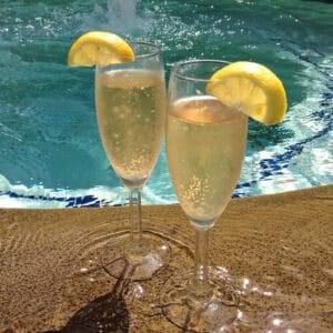 Two champagne flutes of Limoncello Champagne Aperitifs garnished with a lemon slice with a pool in the background