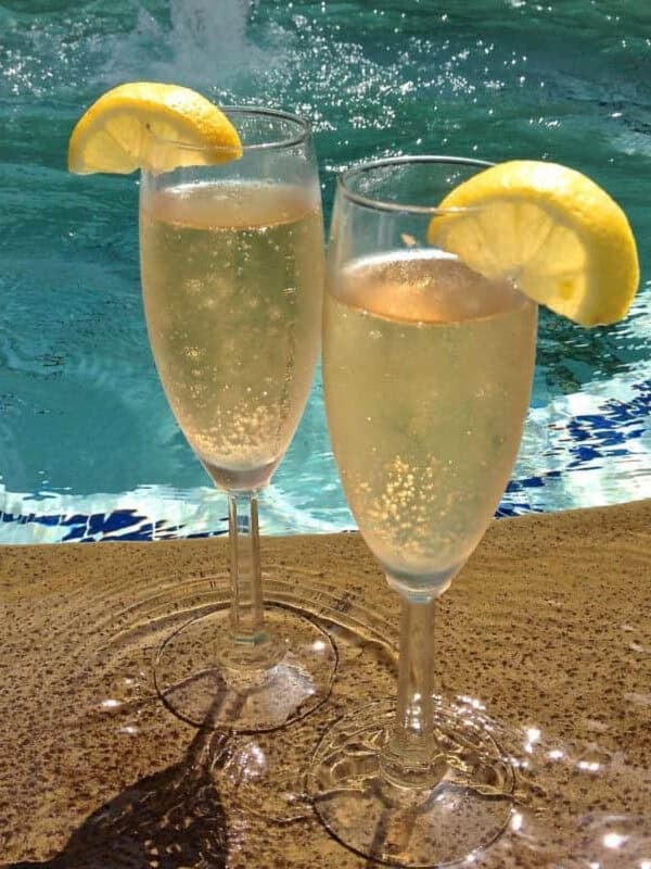 Two champagne flutes of Limoncello Champagne Aperitifs garnished with a lemon slice with a pool in the background