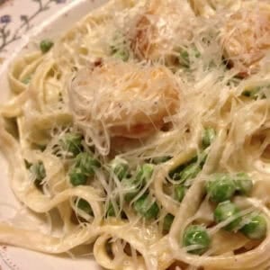 A closeup of a bowl of Creamy Fettuccine with Scallops and Peas topped with grated parmesan cheese