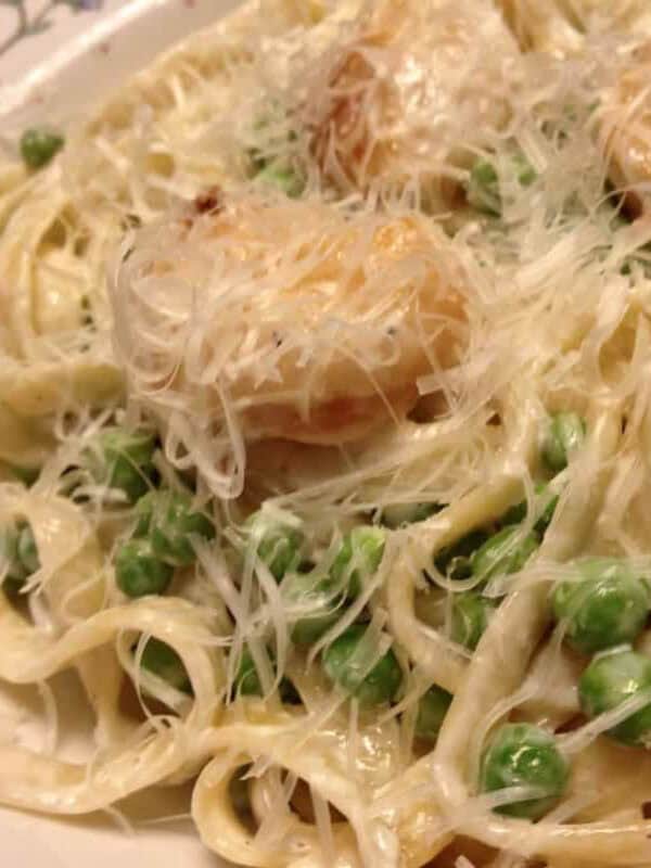 A closeup of a bowl of Creamy Fettuccine with Scallops and Peas topped with grated parmesan cheese