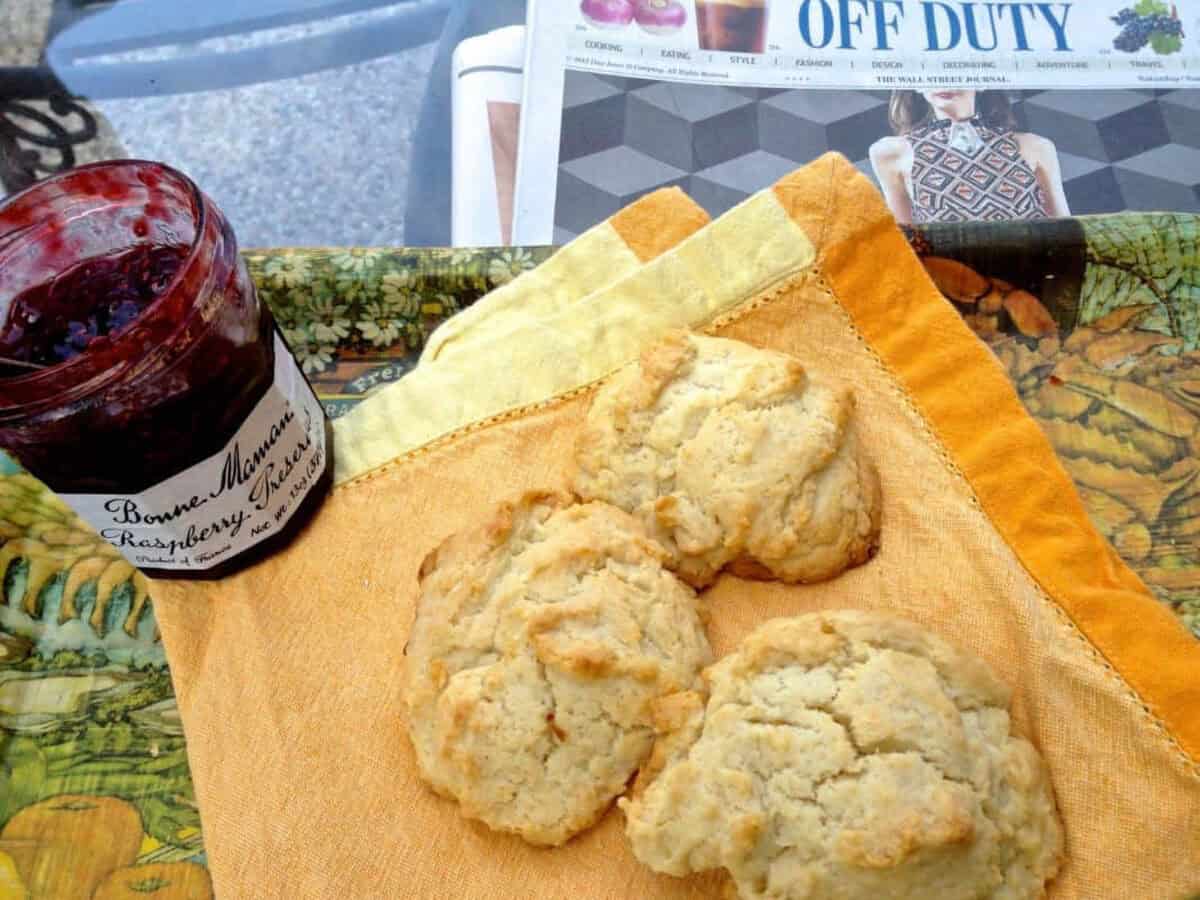 Easy Drop Biscuits via zagleft 3 Overhead view of three Drop Biscuits on a yellow cloth napkin next to a jar of raspberry preserves