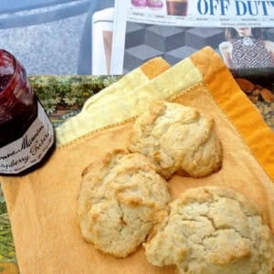 Overhead view of three Drop Biscuits on a yellow cloth napkin next to a jar of raspberry preserves