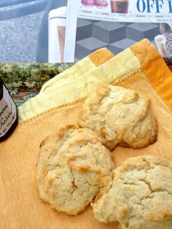 Overhead view of three Drop Biscuits on a yellow cloth napkin next to a jar of raspberry preserves