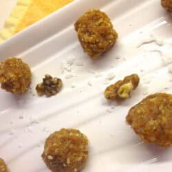 A closeup of six Fruity Nut Balls with scattered shredded coconut and chopped walnuts on a plate