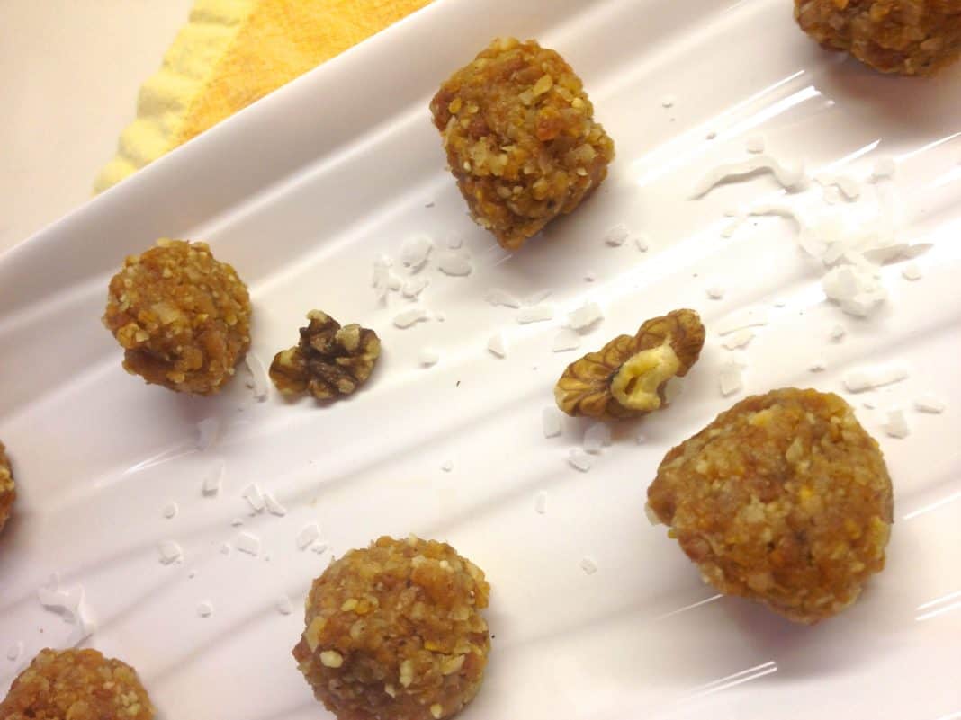A closeup of six Fruity Nut Balls with scattered shredded coconut and chopped walnuts on a plate