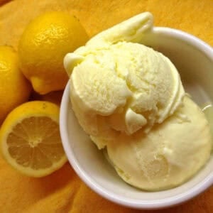 Overhead view of two scoops of limoncello ice cream in a small bowl next to two and a half lemons all on a bright yellow cloth napkin