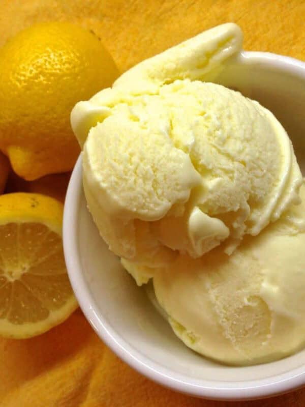 Overhead view of two scoops of limoncello ice cream in a small bowl next to two and a half lemons all on a bright yellow cloth napkin