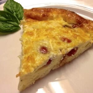 A slice of Roasted Tomato and Feta Crustless Quiche on a plate garnished with three basil leaves