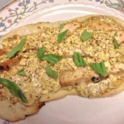 Baked Rosemary, olive oil and sea salt pizza dough topped with melted cheese, grilled chicken strips, and basil on a large plate
