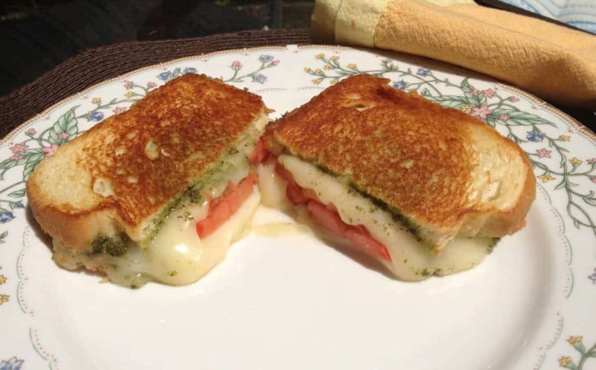 Grilled Mozzarella, Tomato and Basil Pesto Sandwich from Zagleft - 1 Grilled Fresh Mozzarella, Tomato and Pesto Sandwich cut in half on a plate
