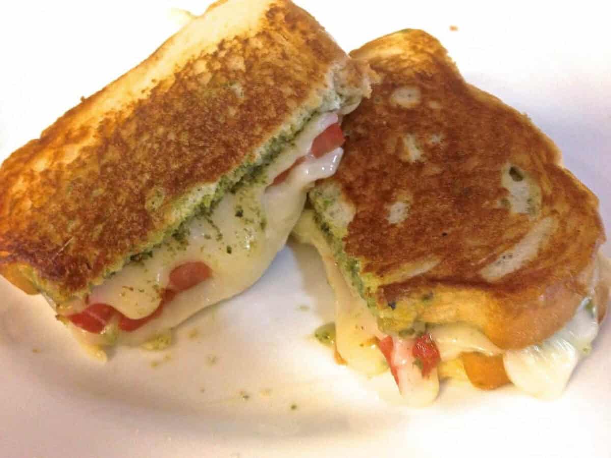Grilled Mozzarella, Tomato and Basil Pesto Sandwich from Zagleft - 3 Overhead view of Grilled Fresh Mozzarella, Tomato and Pesto Sandwich cut in half with cheese oozing from the sides on a plate