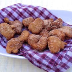 Banana Beignets coated in cinnamon sugar on top of a red and white checkered cloth napkin in an oval-shaped dish