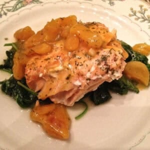 Salmon topped with apricot ginger glaze on a bed of sautรฉed spinach on a large plate