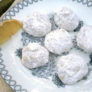 An overhead view of a plate of six Lemon Drop Cookies coated in powdered sugar and garnished with a lemon slice
