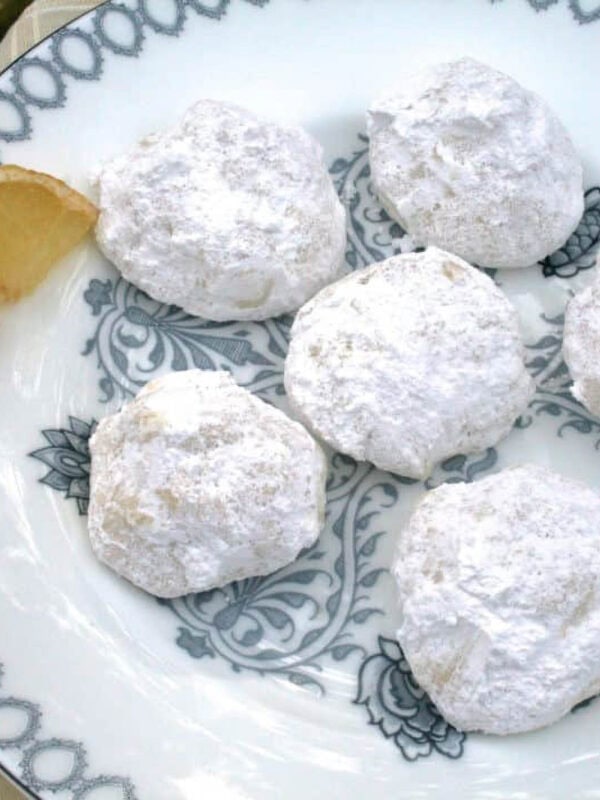 An overhead view of a plate of six Lemon Drop Cookies coated in powdered sugar and garnished with a lemon slice