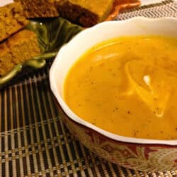 A bowl of Roasted Red Pepper and Butternut Soup next to a plate of beer bread