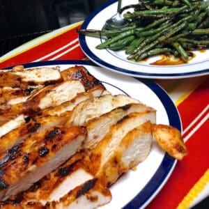 A plate of sliced Honey Sriracha Glazed Chicken next to a plate of roasted green beans