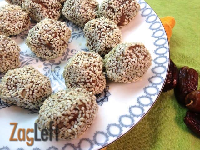 A closeup of a plate of Almond Butter Energy Bites coated with sesame seeds and next to a handful of dates