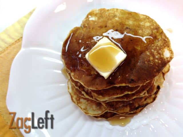 An overhead view of a stack of six pancakes topped with syrup and butter on a plate