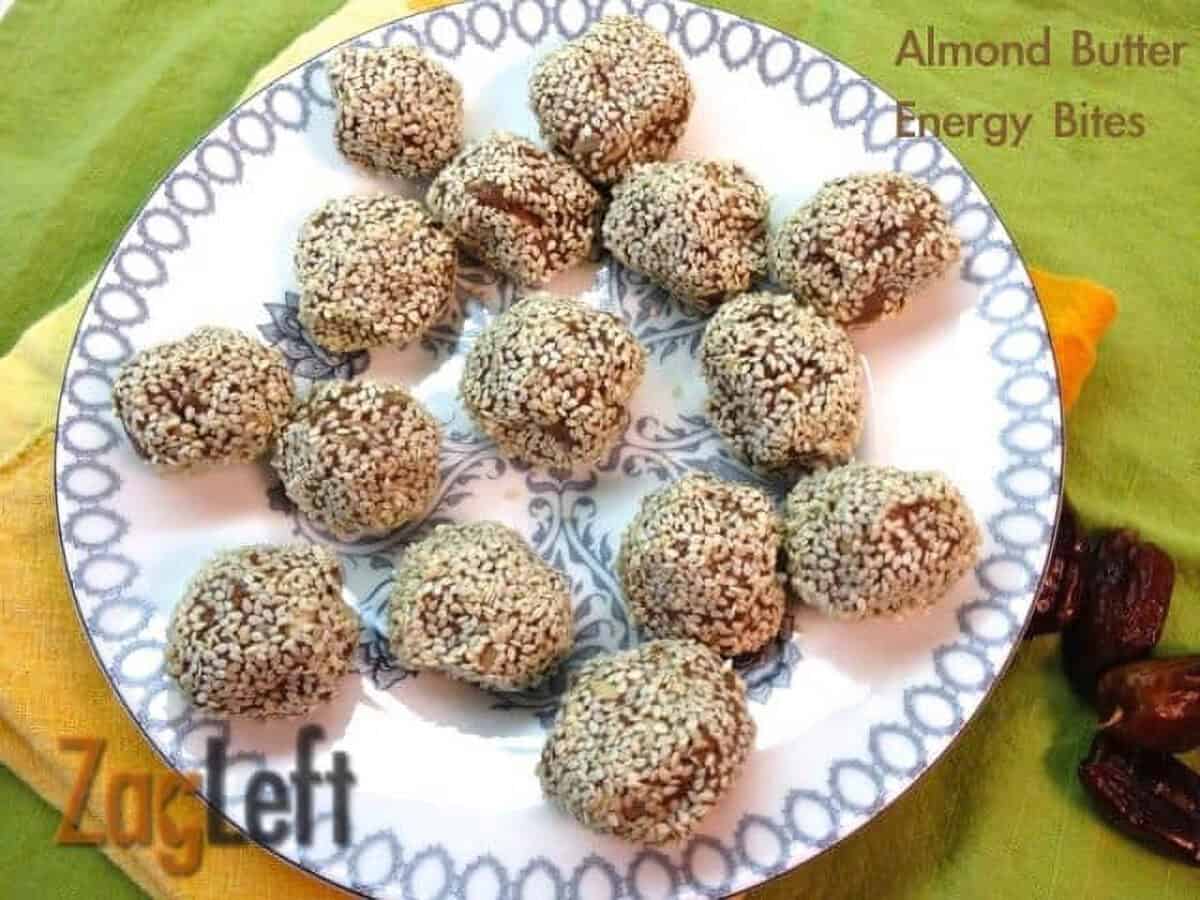 An overhead view of a plate of fifteen Almond Butter Energy Bites coated with sesame seeds next to a handful of dates