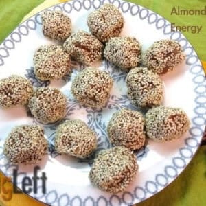 An overhead view of a plate of fifteen Almond Butter Energy Bites coated with sesame seeds next to a handful of dates
