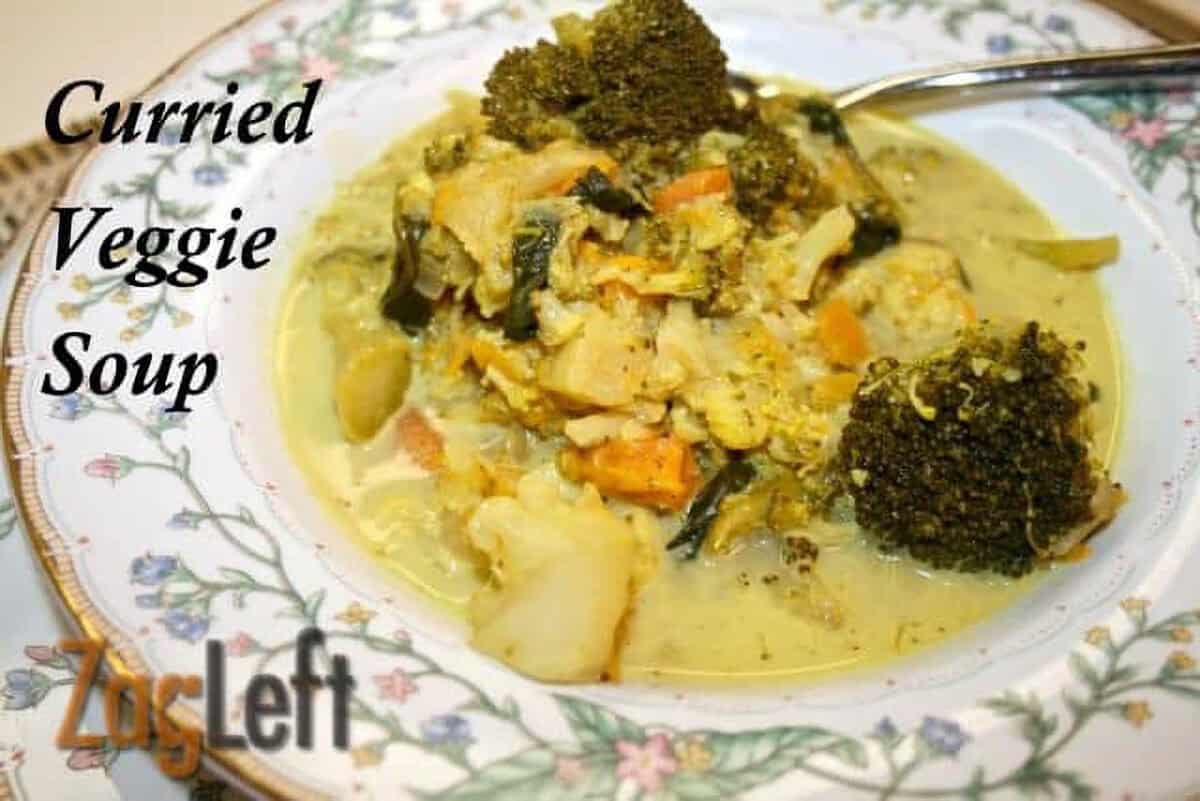A bowl of Curried Veggie Soup with thick pieces of cauliflower, broccoli, carrots, sweet potatoes, spinach and sweet apples.