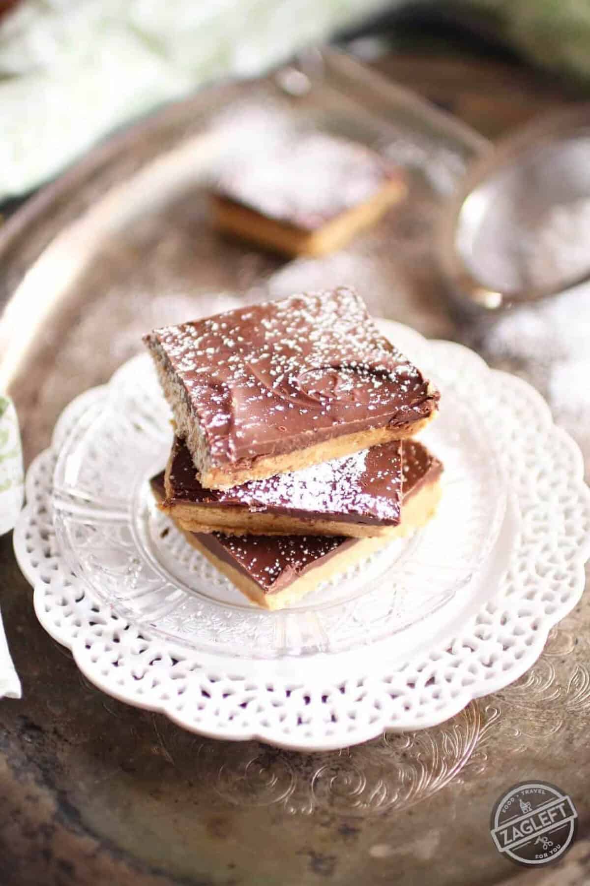 A stack of three No Bake Chocolate Peanut Butter Bars dusted with powdered sugar on a small plate on a metal tray