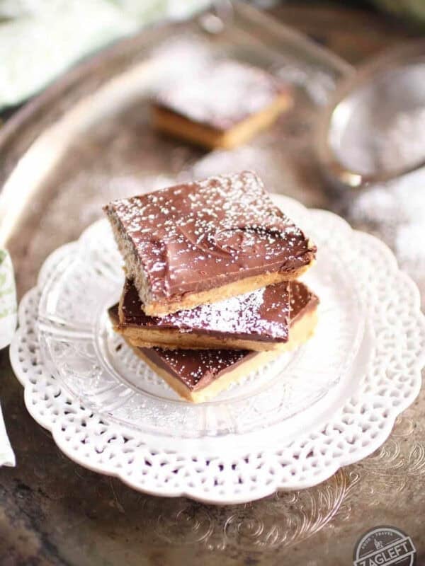 A stack of three No Bake Chocolate Peanut Butter Bars dusted with powdered sugar on a small plate on a metal tray