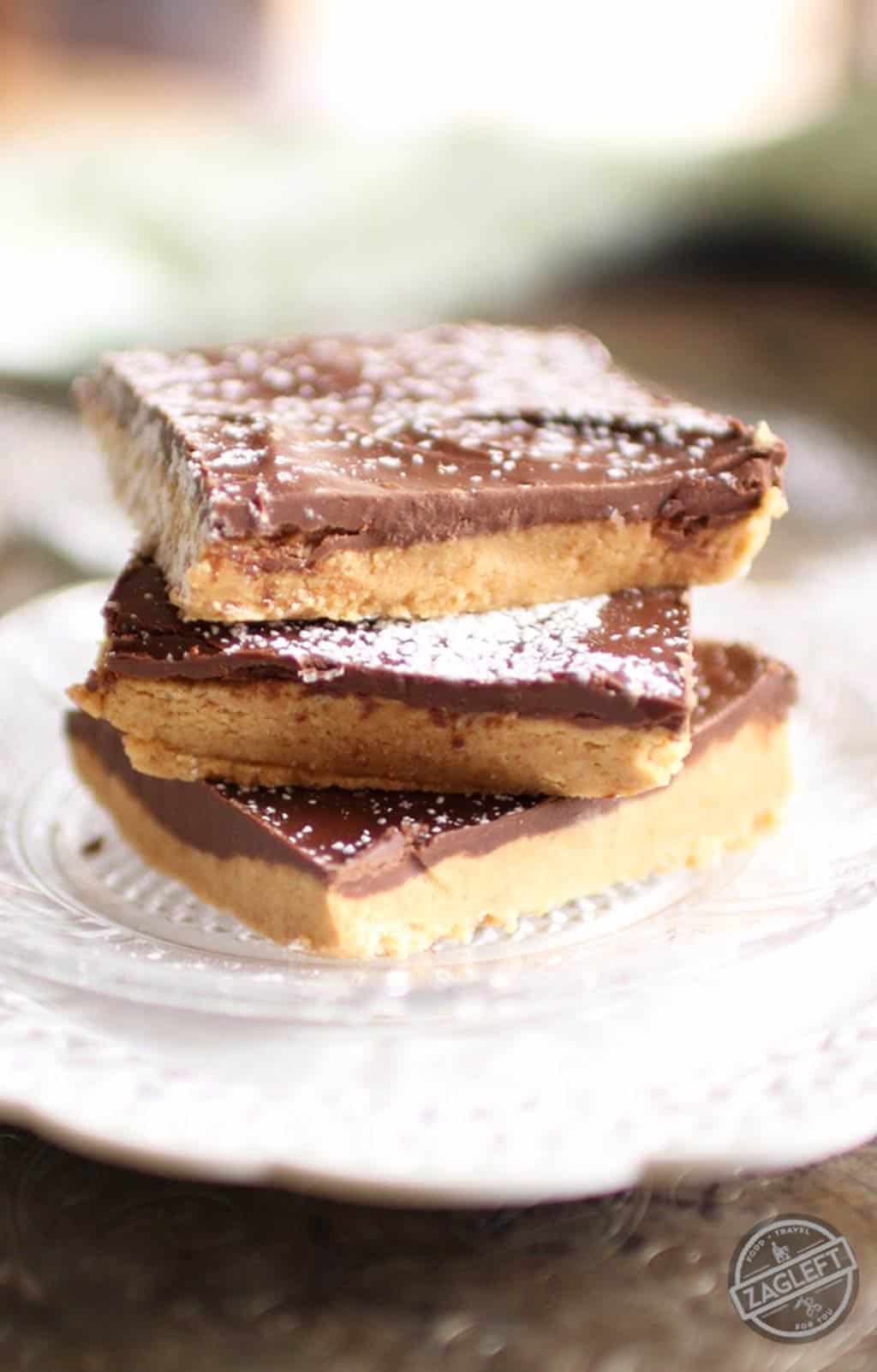 A stack of three No Bake Chocolate Peanut Butter Bars dusted with powdered sugar on a small plate