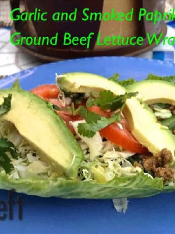 Ground beef lettuce wrap topped with shredded lettuce, three avocado slices, two tomato slices, and cilantro on a large plate