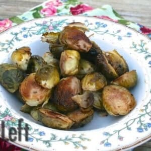 A bowl of Maple Balsamic Roasted Brussels Sprouts on a floral cloth napkin on a wooden surface