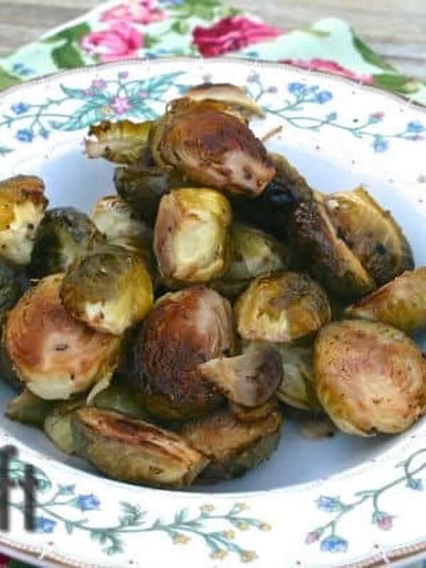 A bowl of Maple Balsamic Roasted Brussels Sprouts on a floral cloth napkin on a wooden surface
