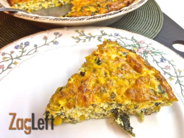 A slice of Roasted Corn and Kale Crustless Quiche on a plate next to the remainder of the quiche in a pie dish 