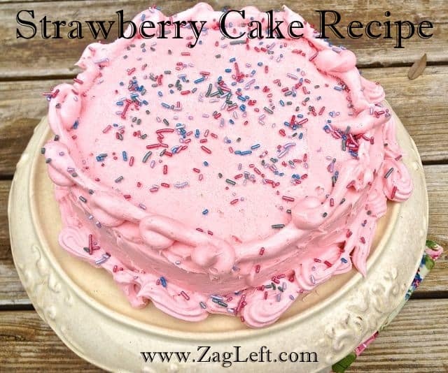 Overhead view of a Strawberry Cake with pink icing topped with purple and pink sprinkles on a cake stand 