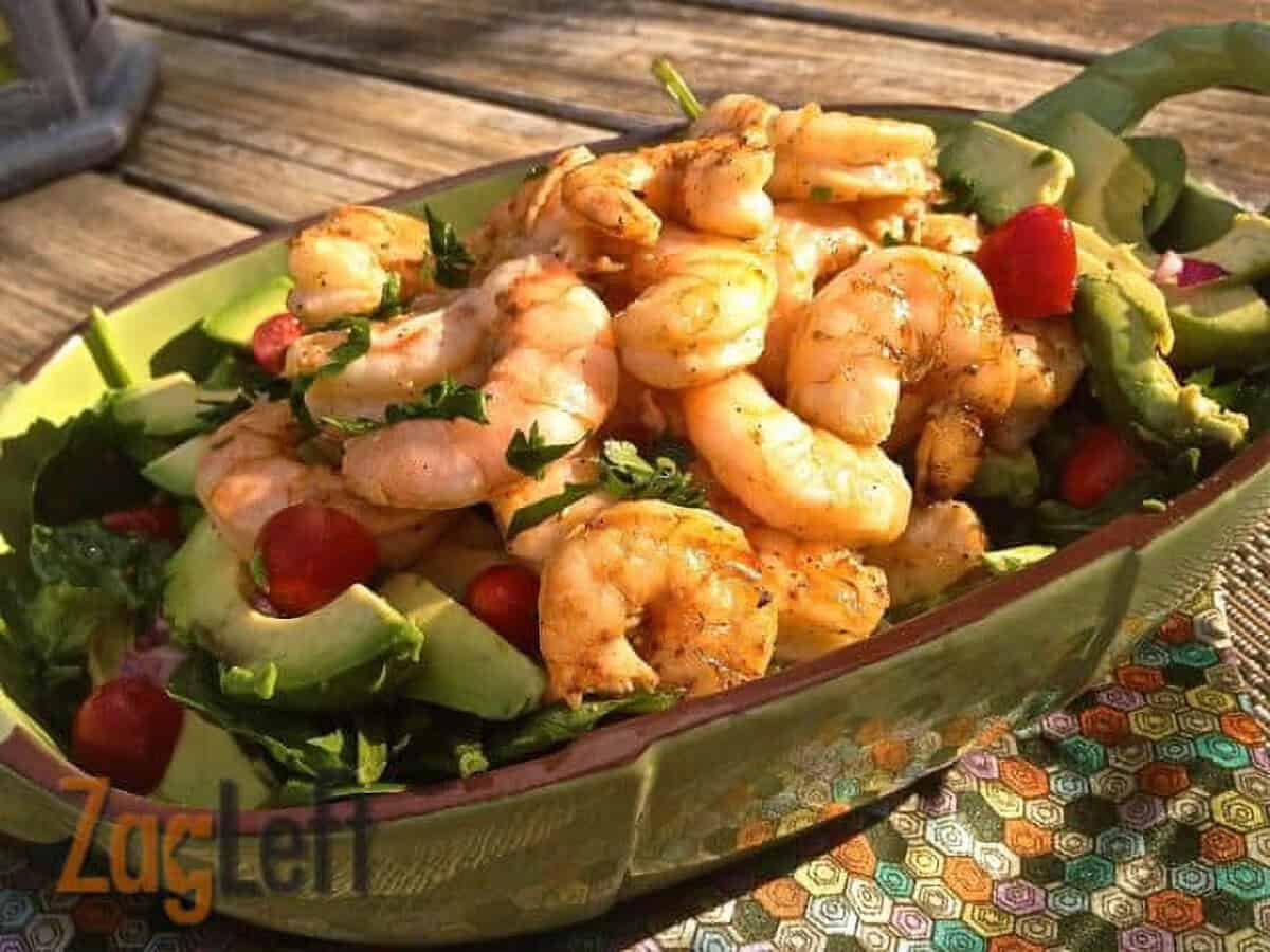 Avocado Salad with cherry tomatoes topped with grilled shrimp in a long green serving dish on a wooden surface