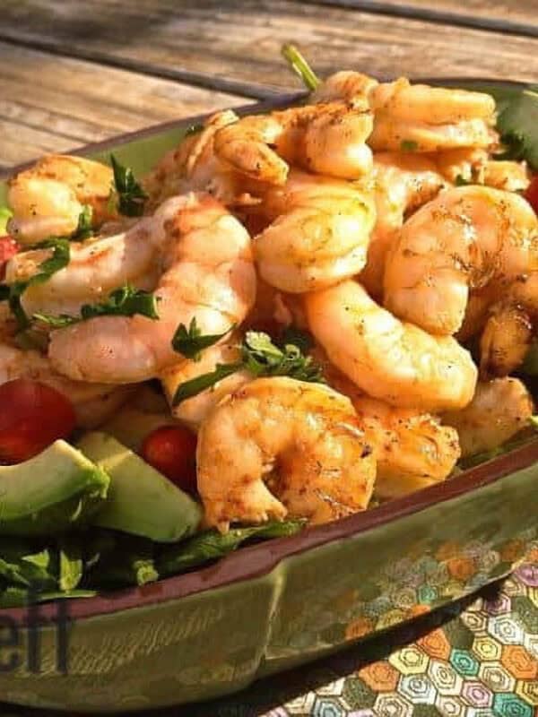 Avocado Salad with cherry tomatoes topped with grilled shrimp in a long green serving dish on a wooden surface