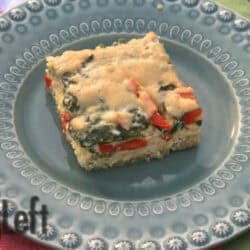A square slice of Baked Quinoa with Spinach, Red Peppers and Cheese on a blue plate next to a fork