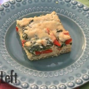 A square slice of Baked Quinoa with Spinach, Red Peppers and Cheese on a blue plate next to a fork