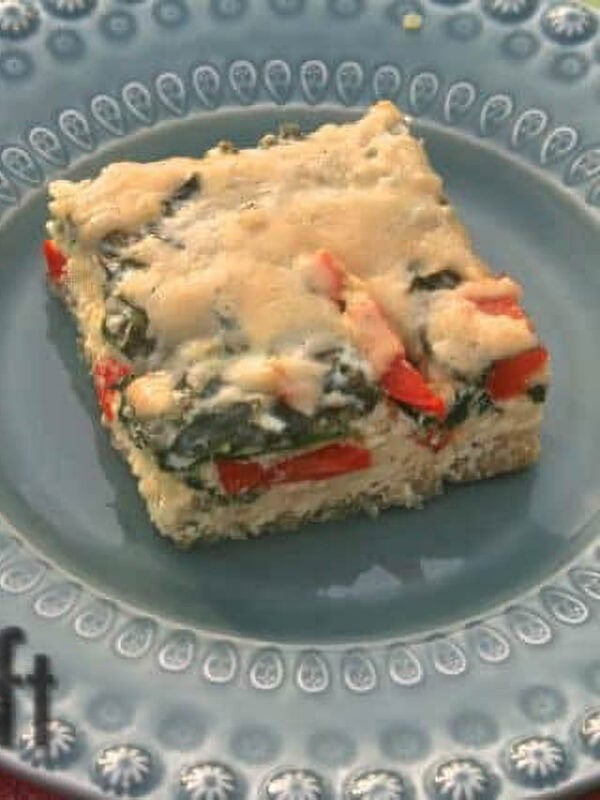 A square slice of Baked Quinoa with Spinach, Red Peppers and Cheese on a blue plate next to a fork