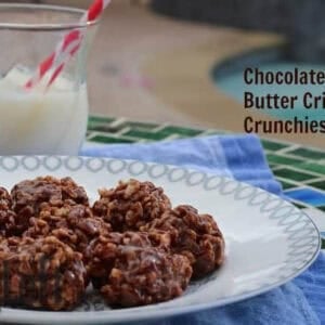 A plate of eight round Chocolate Peanut Butter Crispy Crunchies on a blue cloth napkin, next to a small glass of milk with a red and white striped straw, with a pool in the background