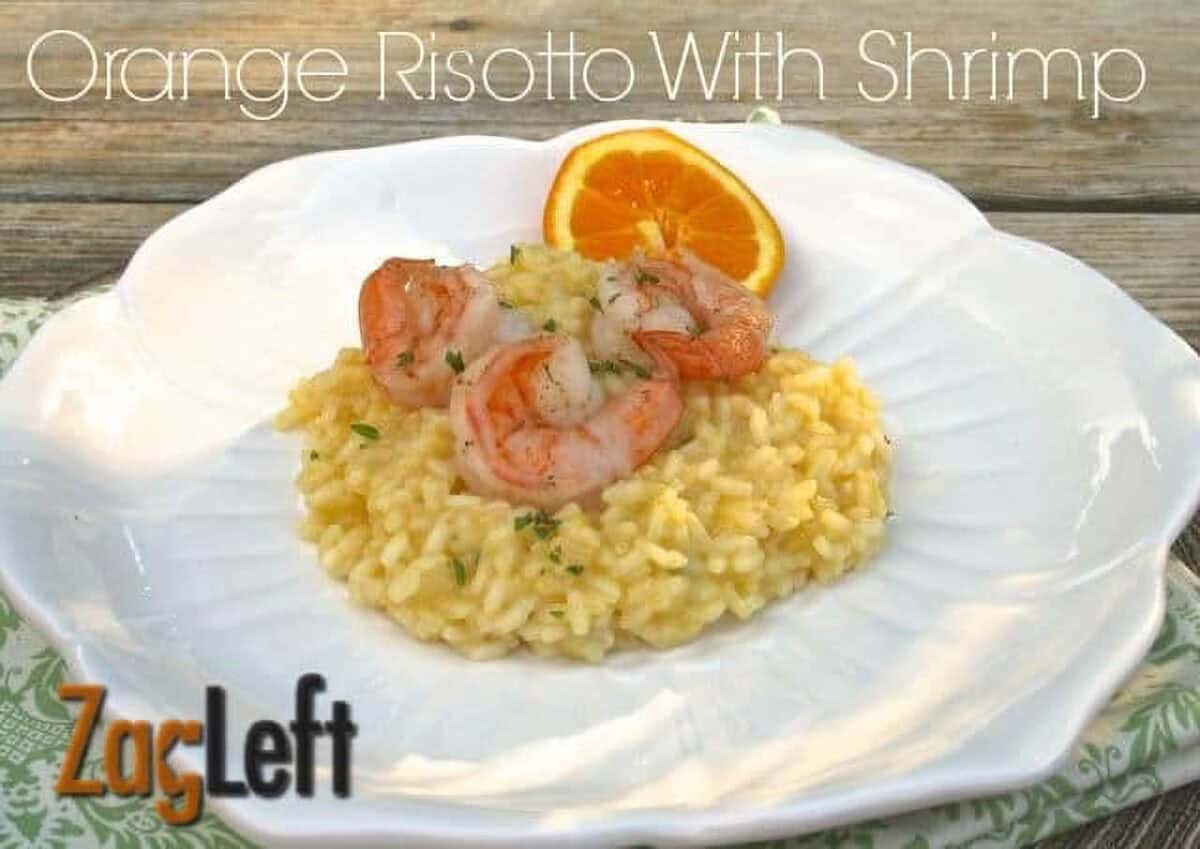 Orange Risotto topped with three pieces of Shrimp on a plate garnished with an orange wheel