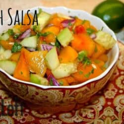 Peach Salsa with cucumbers, red onions, sweet orange peppers, and jalapeños in a bowl plated next to a lime and a half
