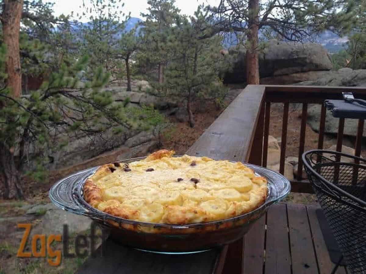A Banana and Chocolate Puffed Pastry in a glass pie dish with a forest in the background
