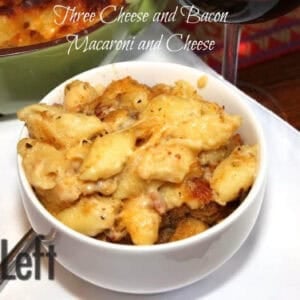A closeup of a bowl of Three Cheese and Bacon Macaroni and Cheese plated next to a glass of red wine and a baking dish with the remainder of the macaroni and cheese