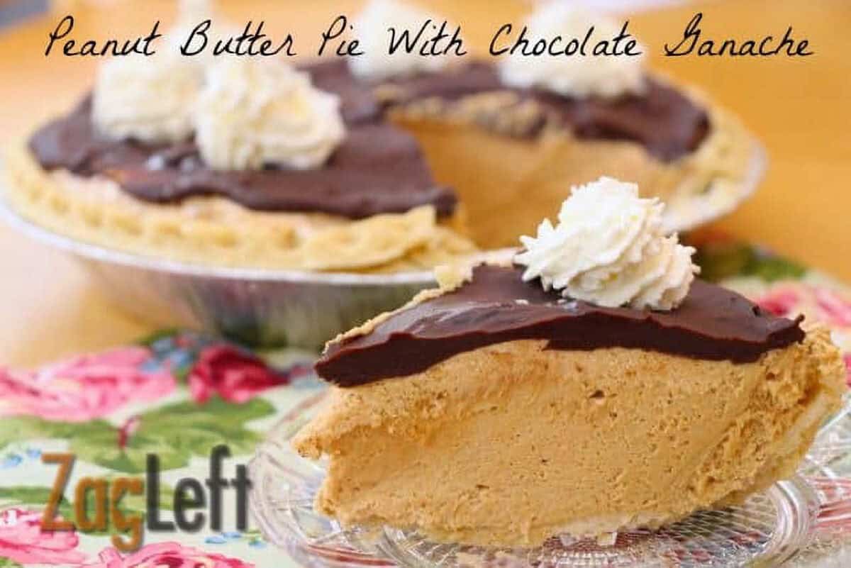 A slice of Peanut Butter Pie topped with a layer of chocolate ganache and a dollop of whipped cream on a small plate on a floral cloth with the remainder of the pie in the background