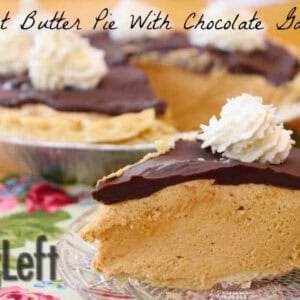 A slice of Peanut Butter Pie topped with a layer of chocolate ganache and a dollop of whipped cream on a small plate on a floral cloth with the remainder of the pie in the background